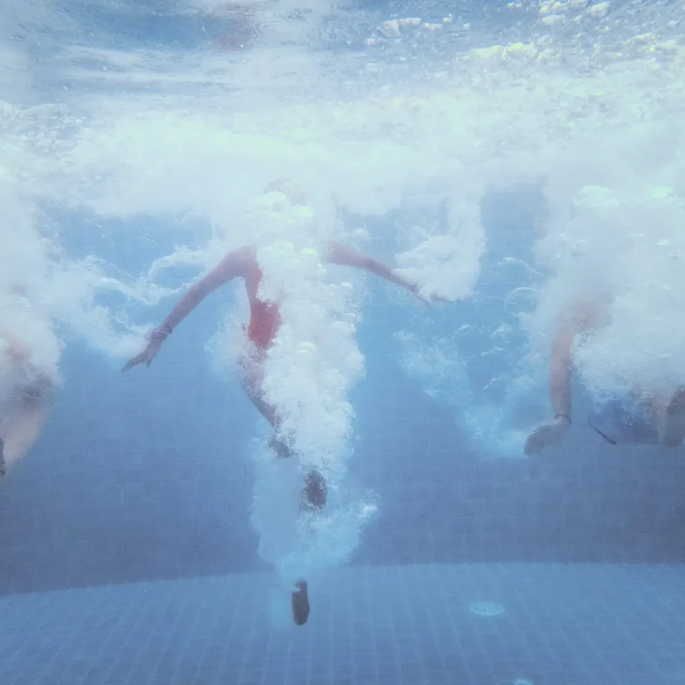 An underwater shot of a group of people jumping down into a swimming pool
